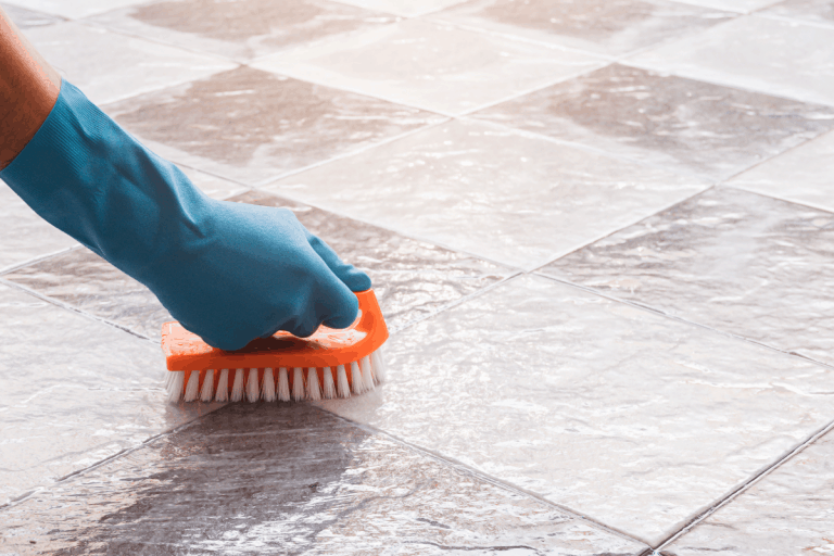 Man wearing blue rubber gloves cleaning the tile floor with scrub, How To Clean Natural Stone Tiles