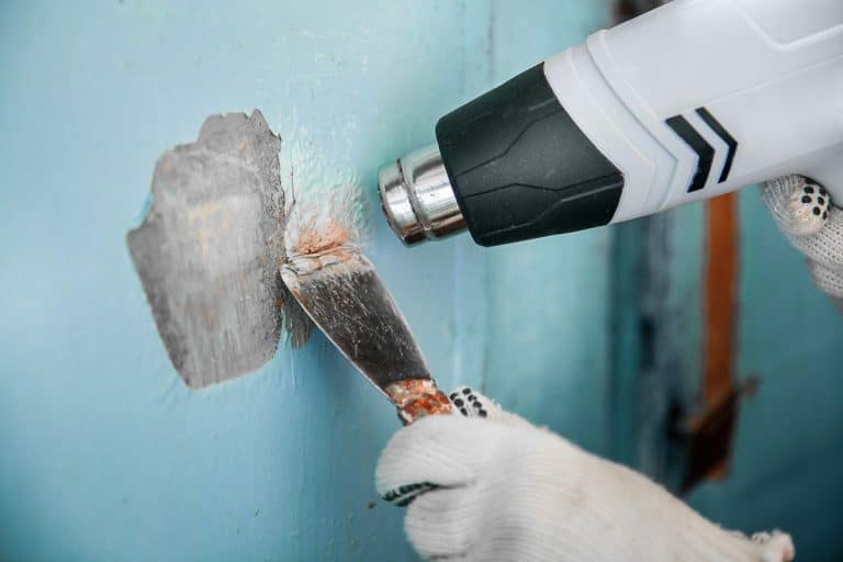 Master removes old paint from concrete wall with heat gun and scraper, How to Remove Paint From Concrete? [5 Simple Steps]