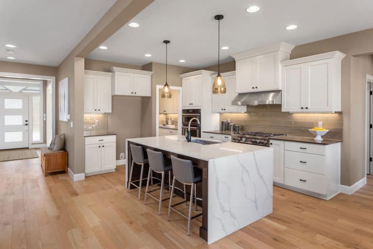 Modern contemporary kitchen area with wooden laminated flooring, marble countertop kitchen island, and white paneled kitchen cabinets, Kitchen Island Vs Breakfast Bar - Which Is Better?