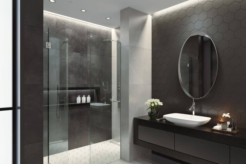 Modern contemporary bathroom with a circular mirror on a dark gray wall and a glass wall shower area