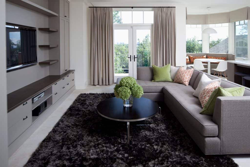 Modern contemporary living room with a dark fur rug, gray sectional sofa, gray tv wall unit with cabinets, and a gray section sofa