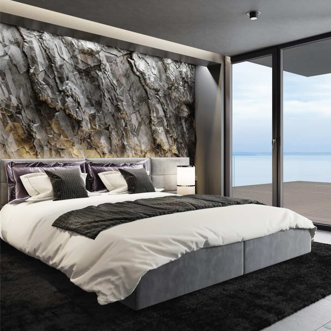 Modern matte black interior with mountain natural stone rock wall, king-size bed with black gloss side tables, black carpet and ceiling with down lighters