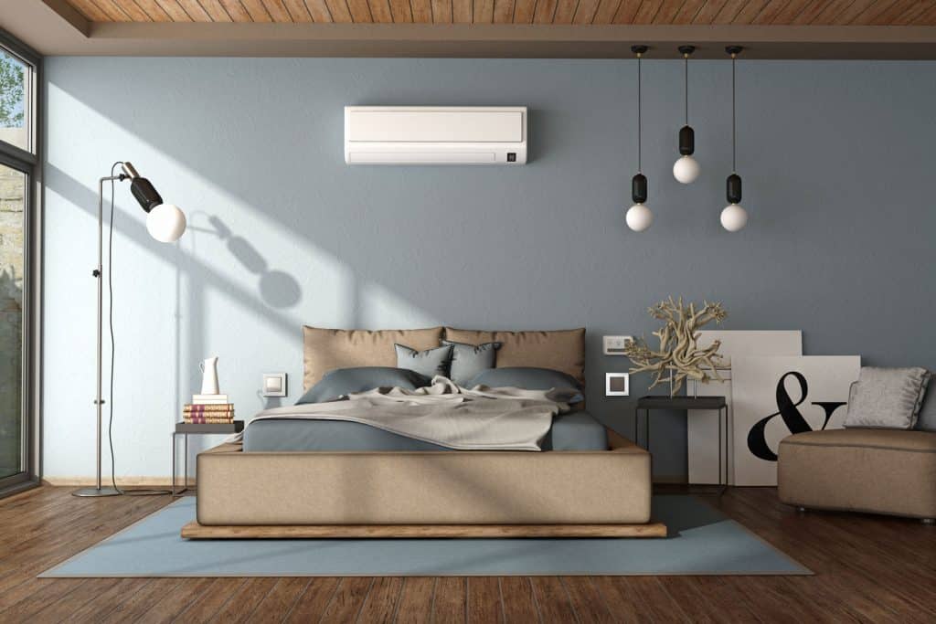 Opaque blue colored walls with air conditioning on the wall and a brown bed with light off-blue colored beddings with a gray blanket