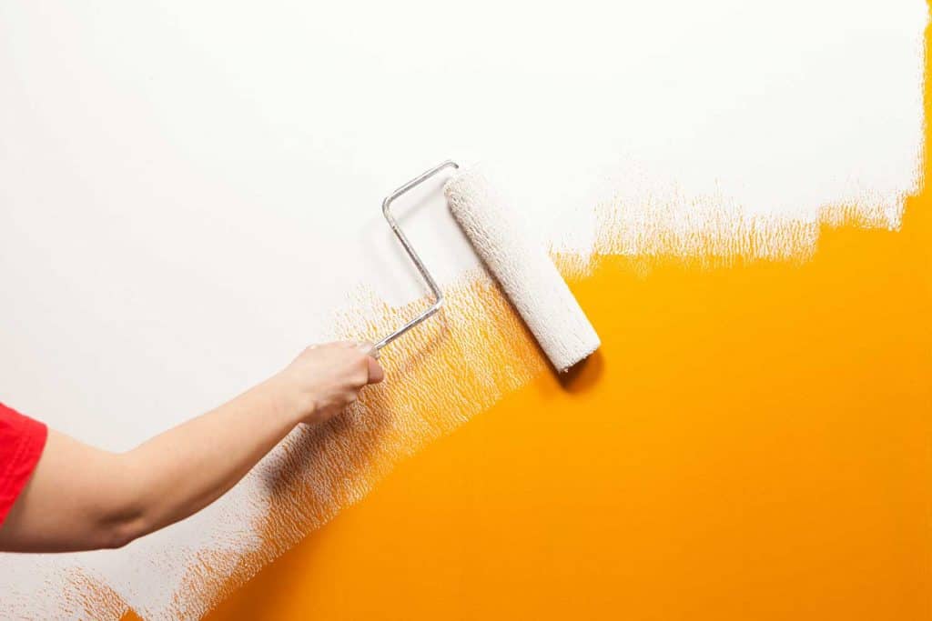 Painter rolling white paint over old orange wall