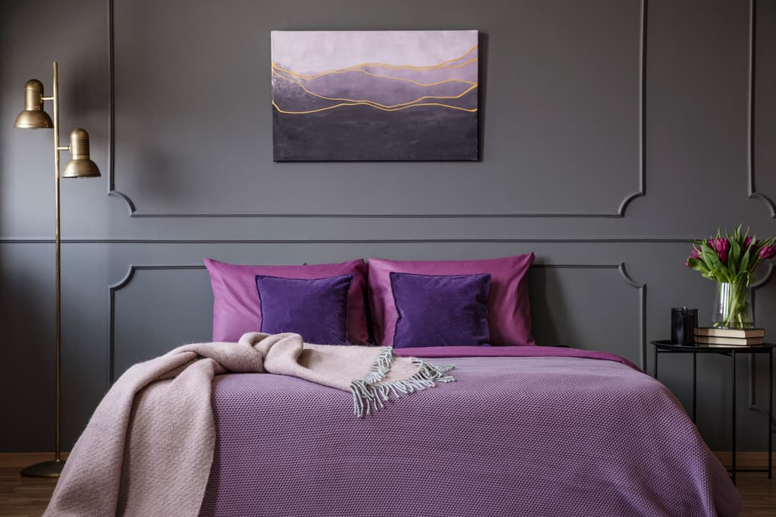 Pink blanket on violet bed in elegant bedroom interior with painting on grey molding wall
