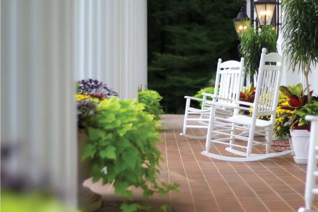 Rocking chairs sitting outside on the front porch of a home with white columns, 5 Best Rocking Chairs And Rocking Benches For Your Porch