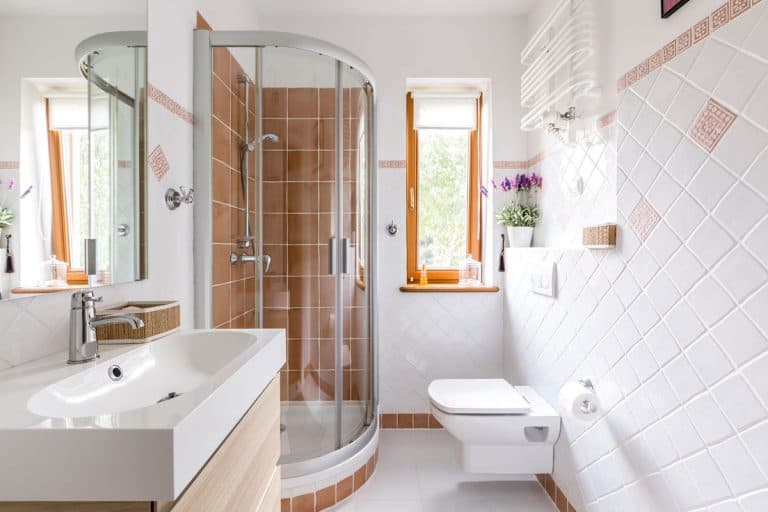 A small modern bathroom with white tiled walls, a mirror, lavatory and a semi circle shower area, What Is A 3/4 Bathroom? (Compared To A Full Bathroom)