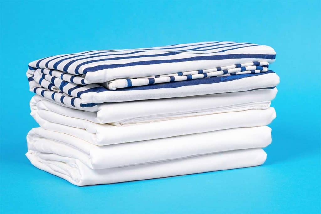 Striped and snowy white bed linen, neatly folded sheets on blue background