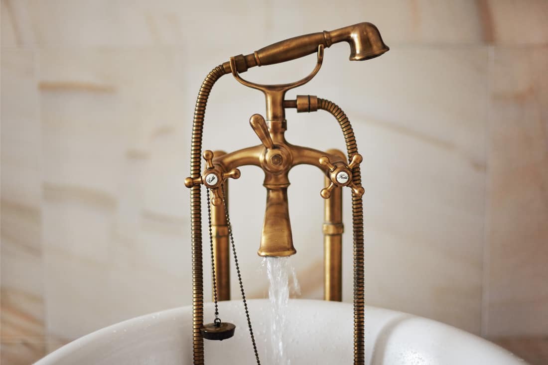 Water running down from antique bronze faucet tap into the bathtub