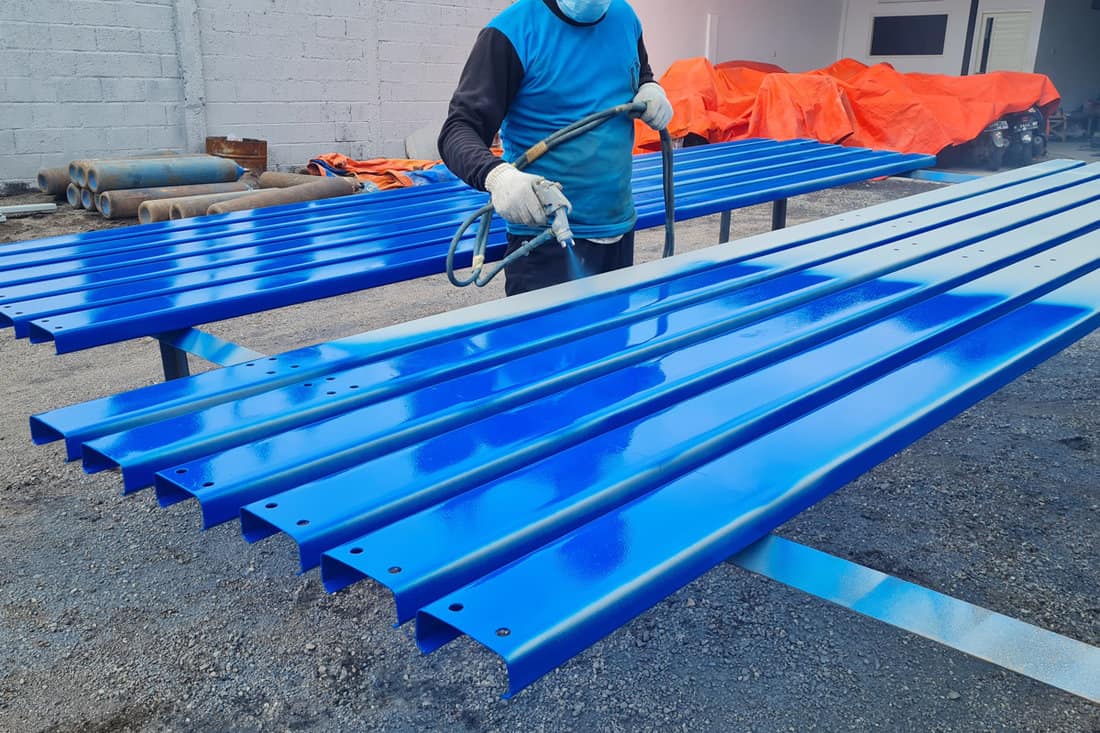 Worker painting metal purlins with a blue color