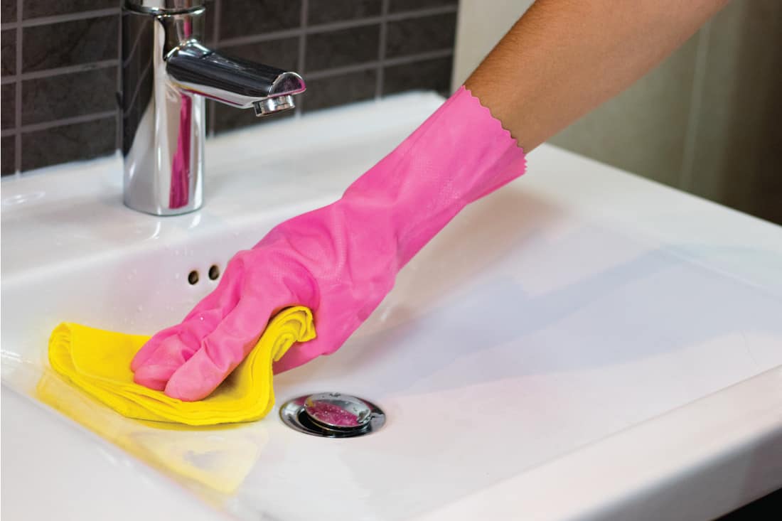 hands in pink gloves using microfiber cloth cleaning bathroom sink with chrome fixtures