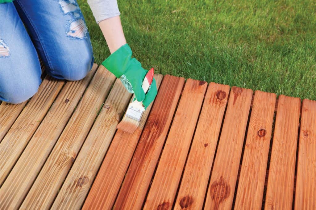 Lady wearing gloves and applying protective varnish on a wooden deck