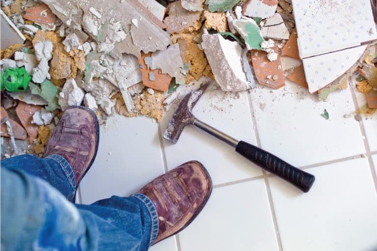 Man standing on broken tiles from a bathroom renovation, How Much Does It Cost To Renovate A Bathroom?