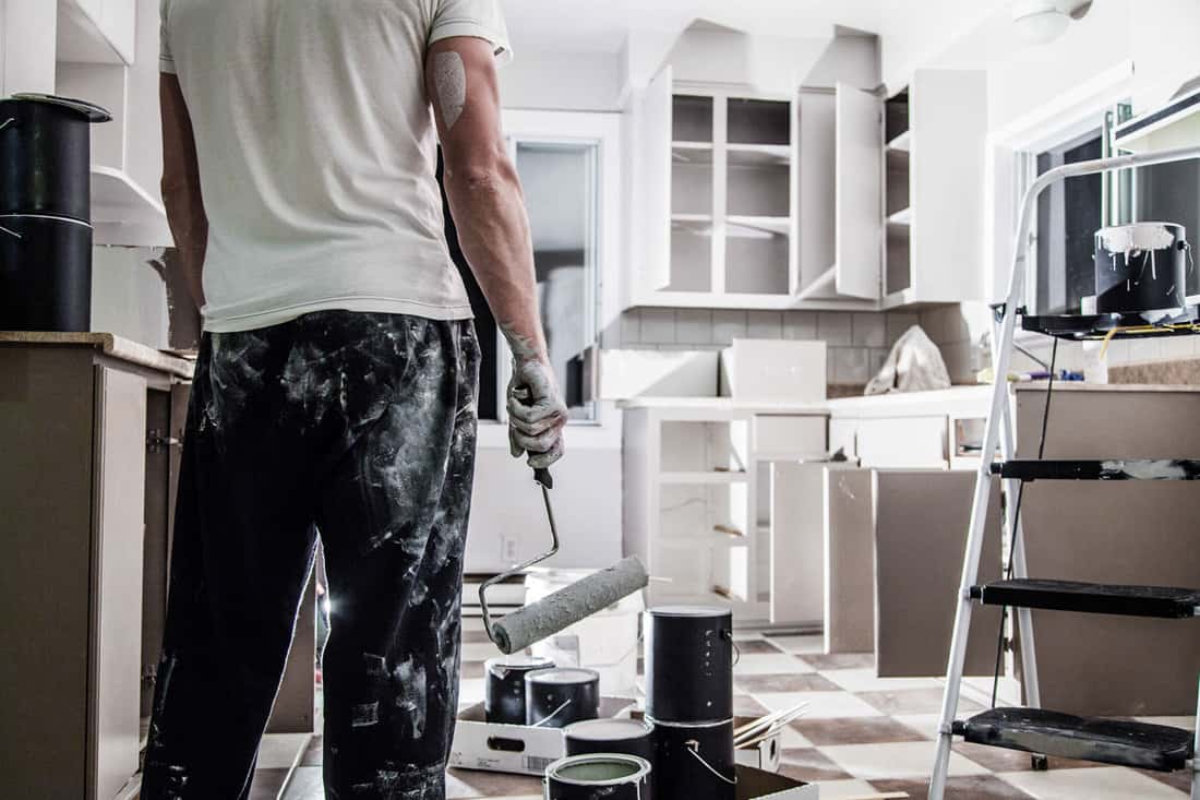 Man holding a paint roller looking at kitchen cabinet paint job