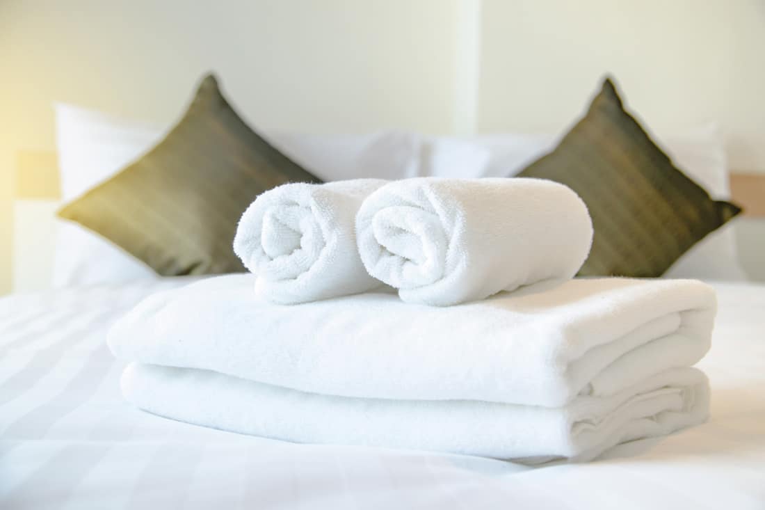 soft white towels rolled on top of a hotel room bed