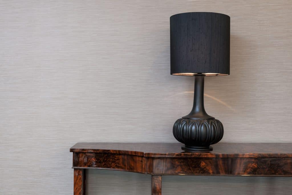 A black colored lampshade on top of a wooden console table