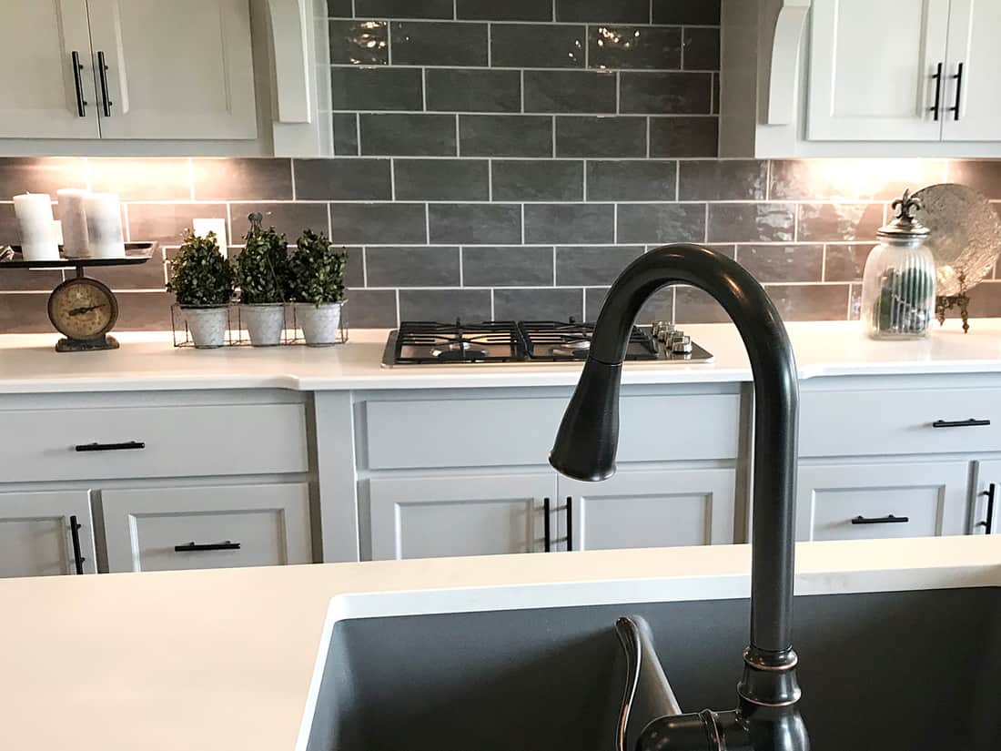 A close up shot of a black faucet in a kitchen island with white cabinets and white countertops
