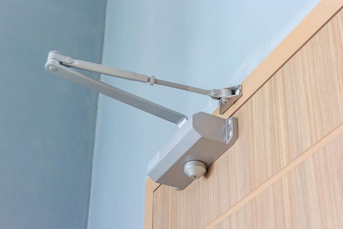 A closing mechanism of a wooden door with blue painted walls, How To Adjust A Screen Door Closer Mechanism