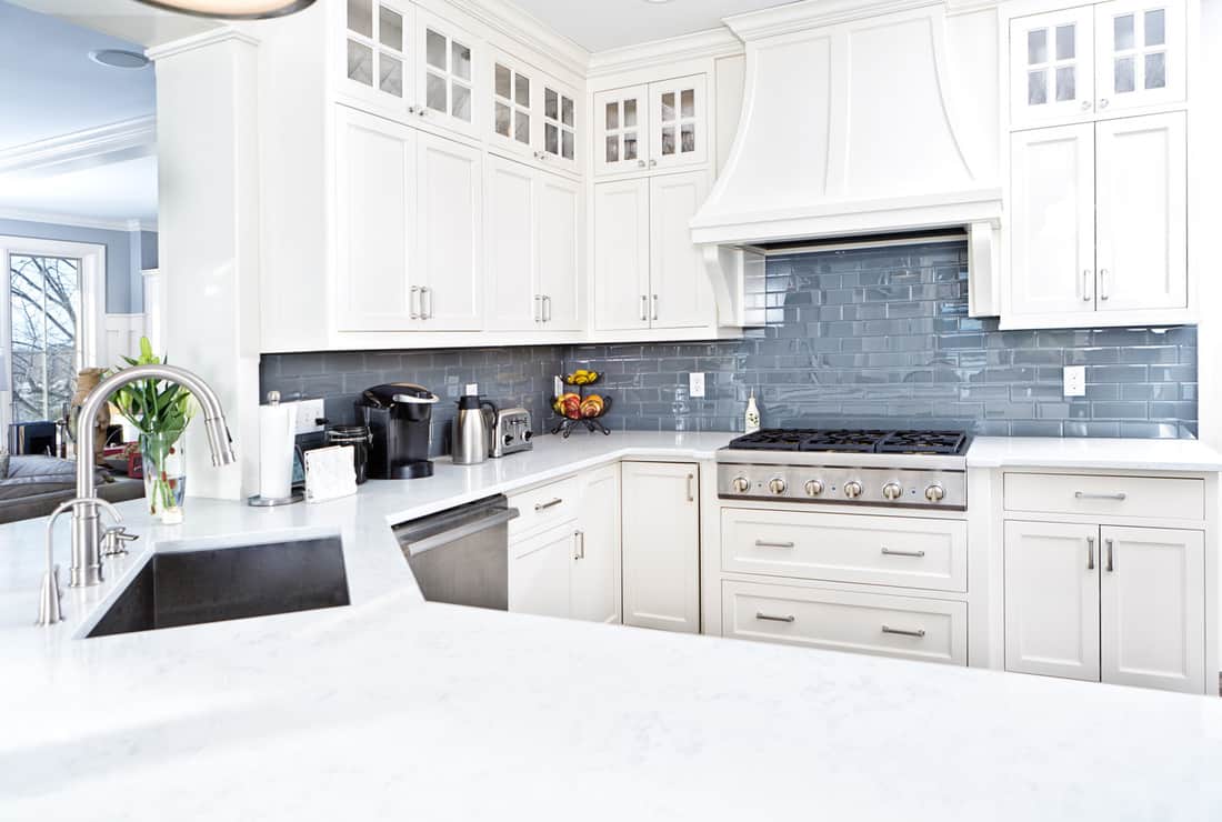 A contemporary home kitchen with stainless steel appliances, painted white cabinets, and quartz countertops