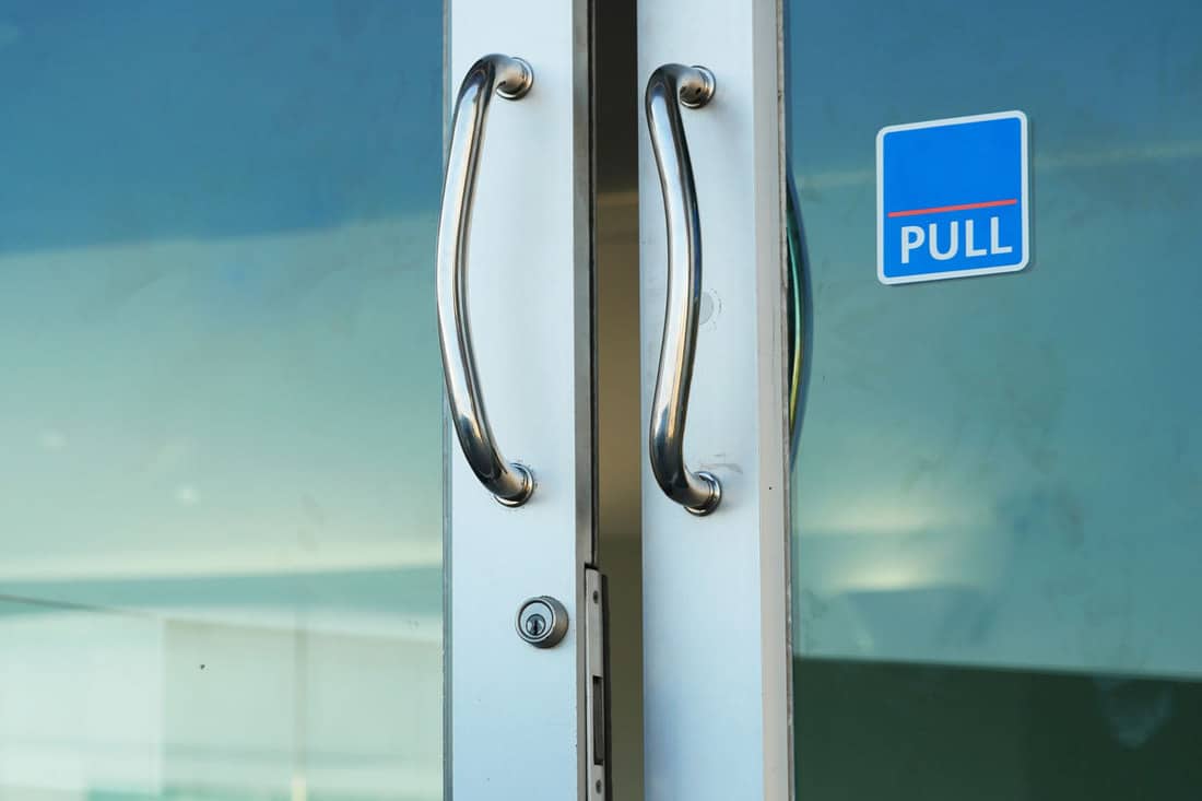 A glass door with modern door handle bars and a pull signage on the right, How To Keep People From Walking Into A Glass Door