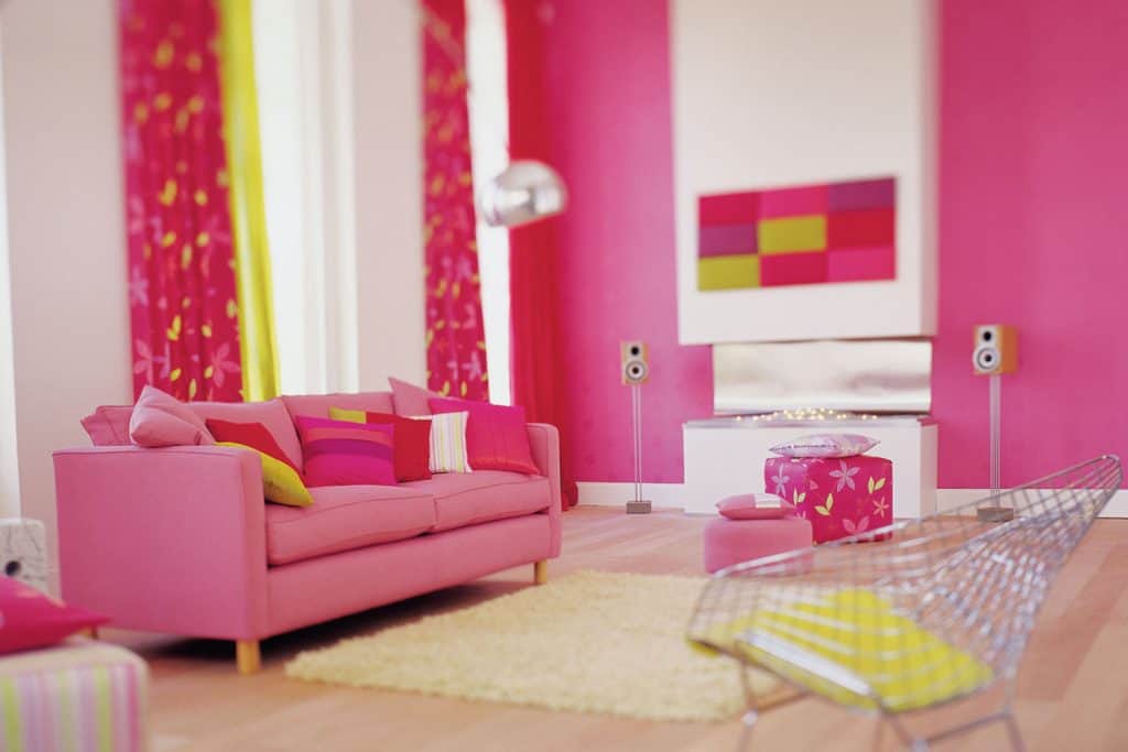 Un magnifique salon aux murs roses avec une cheminée blanche, un canapé rose et des rideaux roses