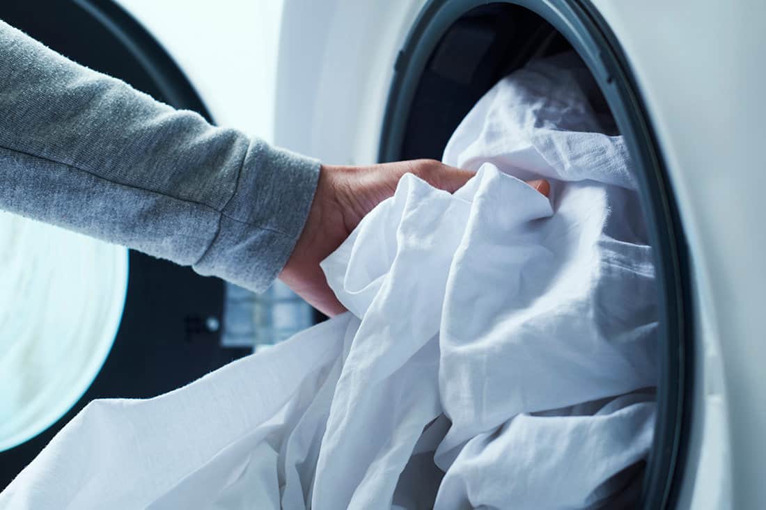 A man put dirty sheets on the washing machine by hand