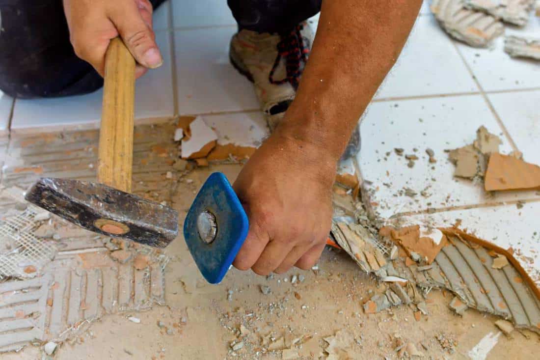 A man removing tile with hammer and chisel scraper, How To Remove Bathroom Tiles (7 Steps)