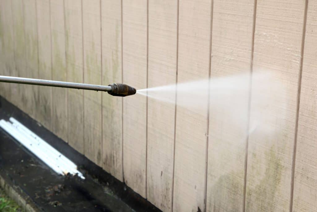A man using a power sprayer to clean the exterior sidings of his house