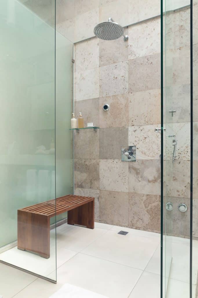 A narrow glass walled shower area with a wooden shower bench on the side
