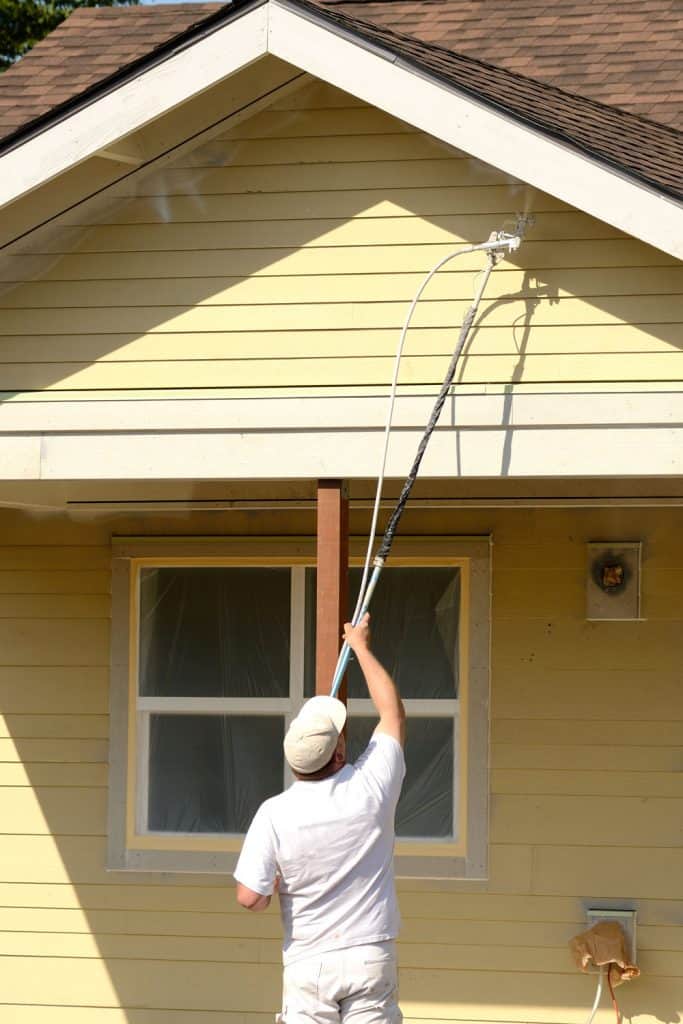 A painter painting the aluminum sidings of a house with a yellow color