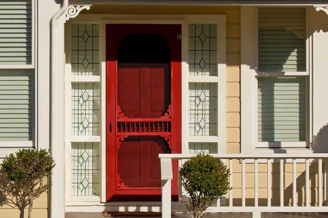 A red door with screen of a simple Victorian-style home with porch, Should the Screen Door Match Your Front Door?