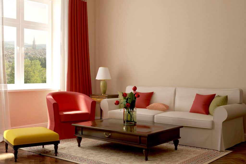 A retro themed living room with a white sofa and a red accent chair inside a beige colored living room