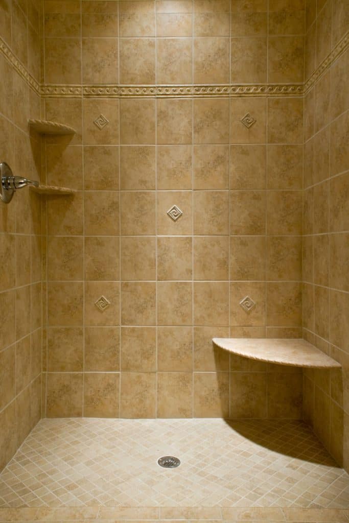 A small shower area with brown tiles and a floating shower bench