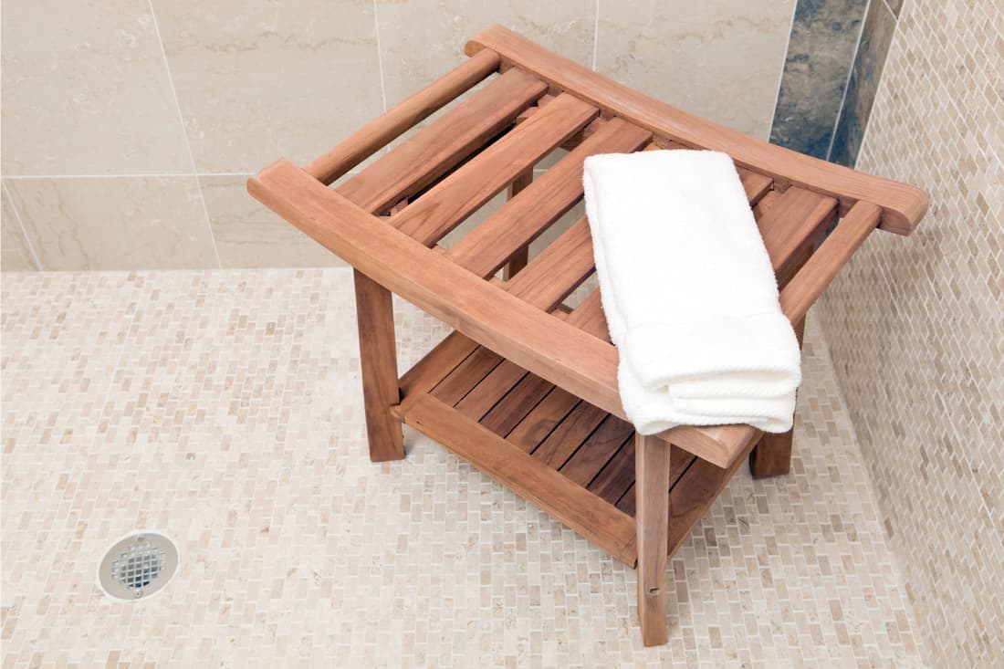 A stained wood shower bench with white towel in a hotel or spa shower