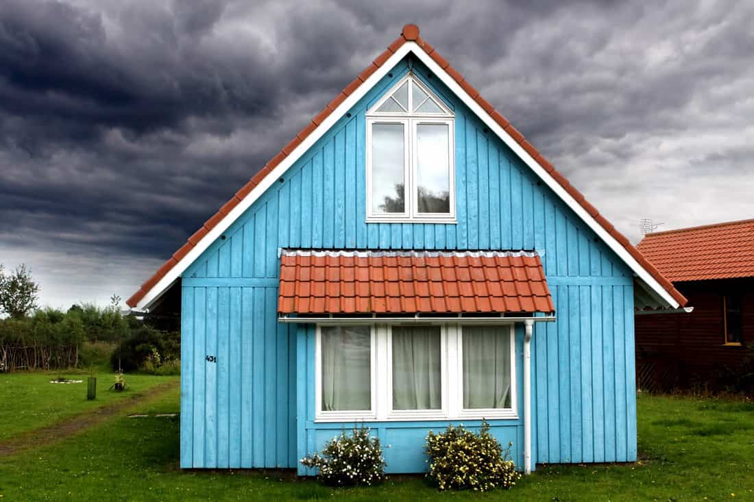A stormy sky surrounds a small and peaceful blue wooden house.