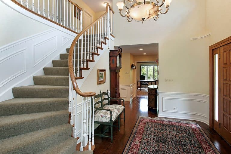 A white color painted wall foyer area, white banisters, and wooden handrail, carpeted stairs steps, and wooden flooring, Should Foyer And Dining Room Lighting Match?