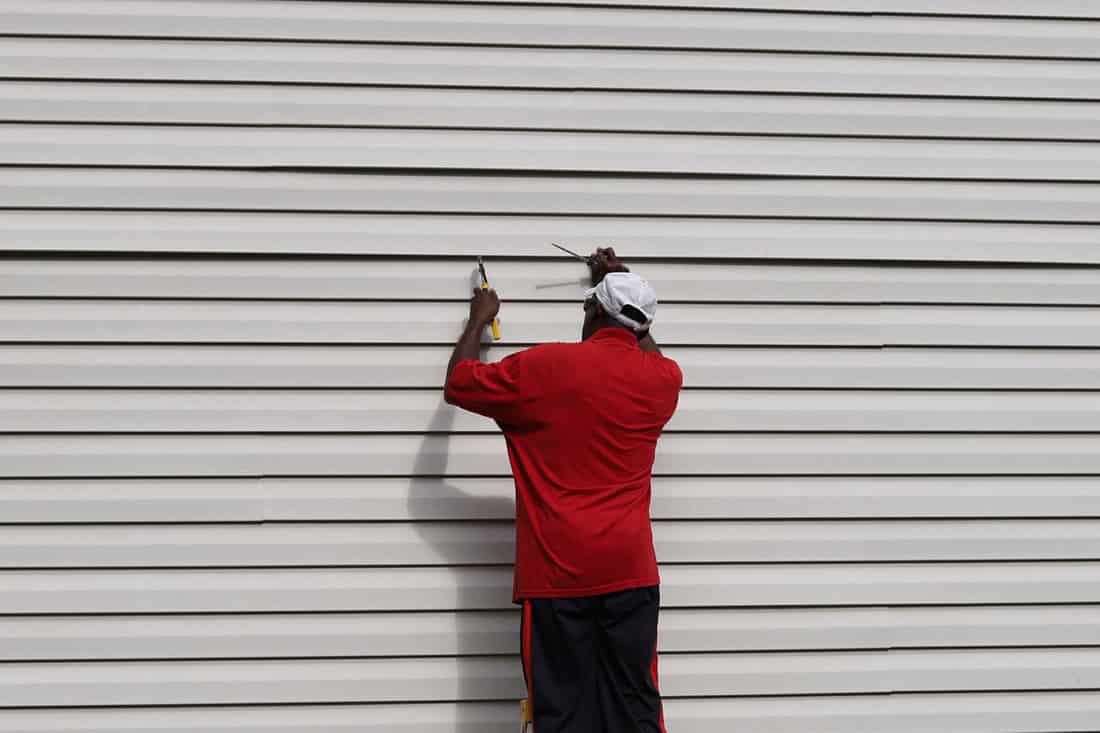 An African-American man on a ladder and fixing cracked vinyl siding on a house, How to Repair Cracked Vinyl Siding?