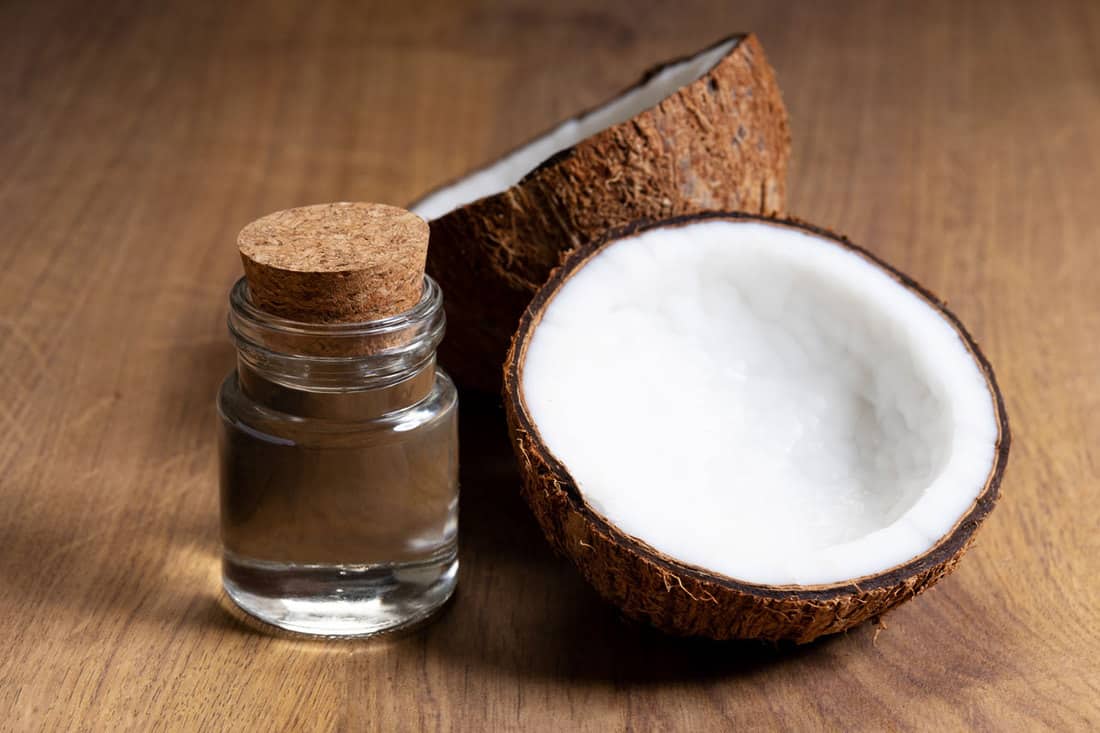 An up close photo of coconut oil and sliced coconut on a wooden table