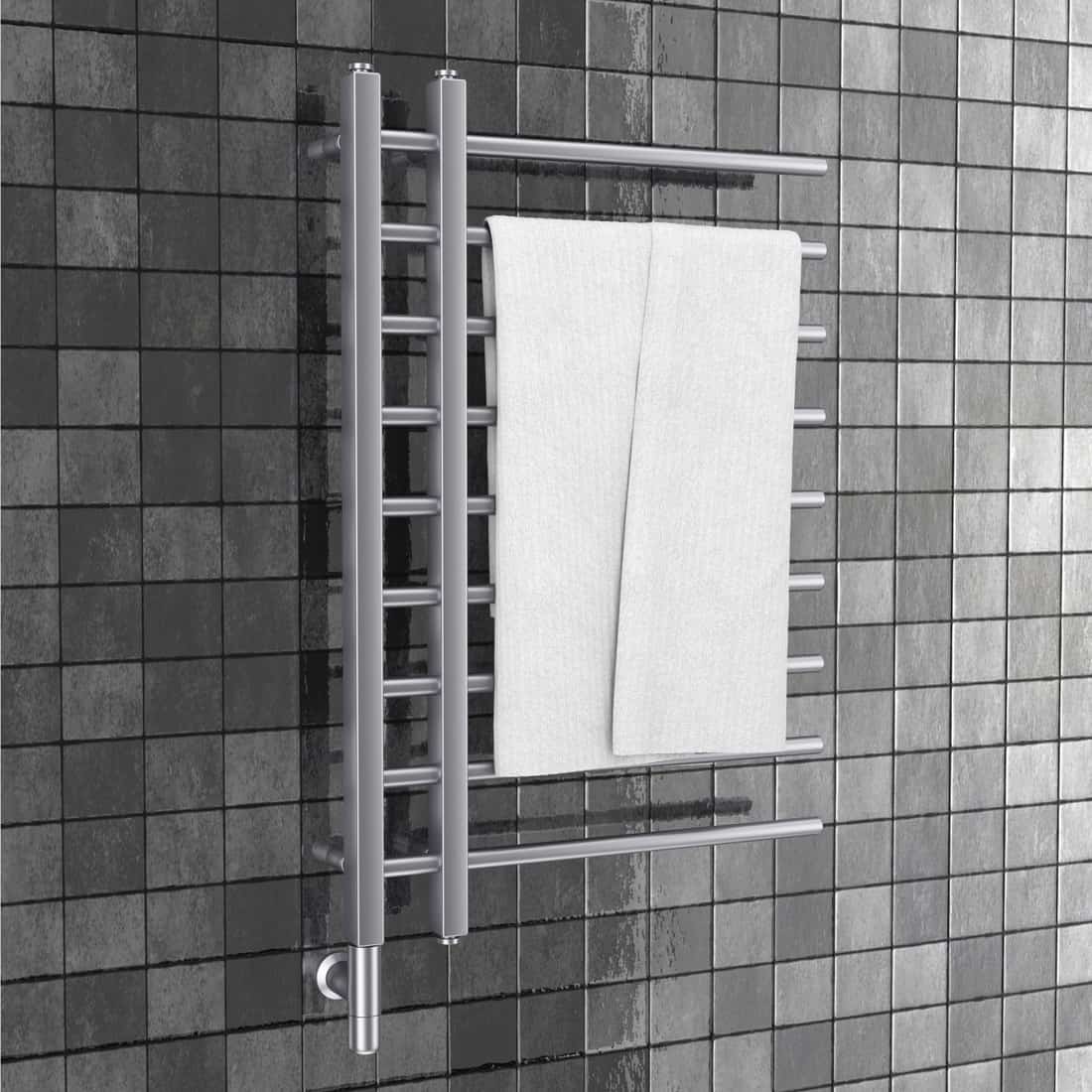 Bathroom towel heater warmer rail with towel in front of gray tiles wall