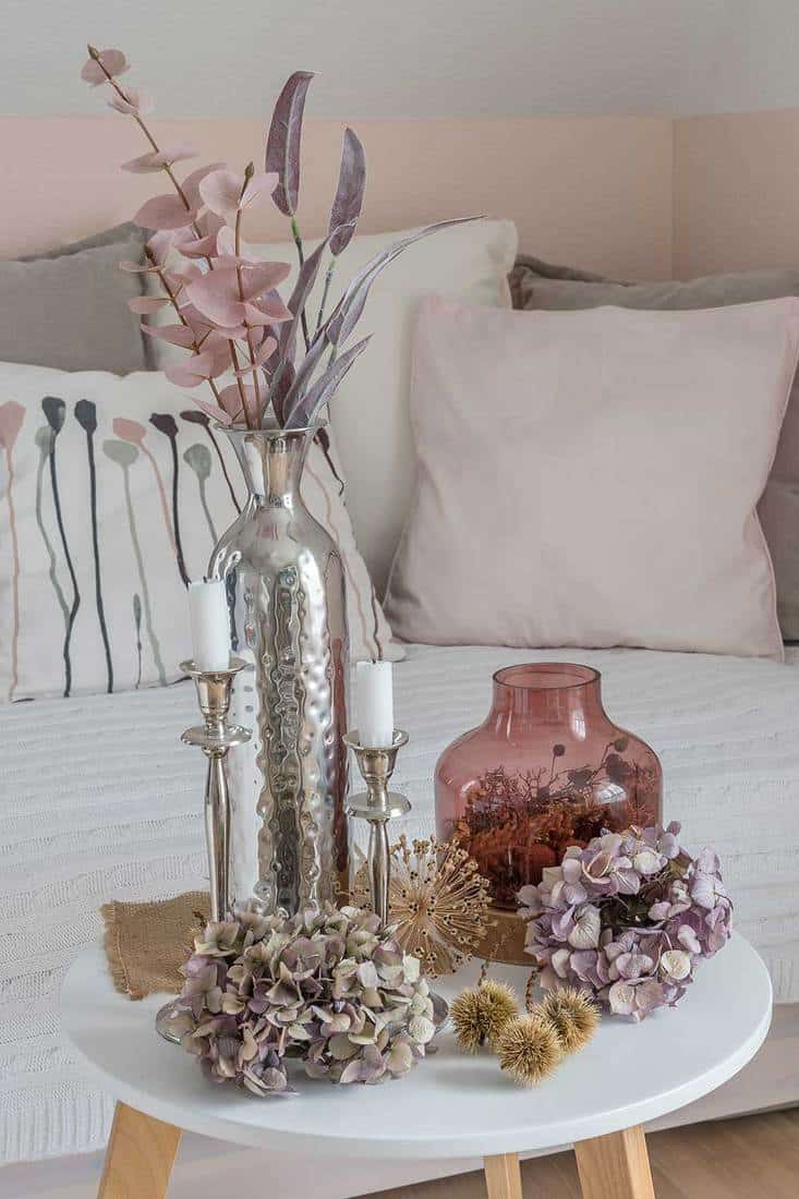 Belle décoration d'automne harmonieuse sur une table basse avec des fleurs d'hortensia séchées, des bols en châtaignier, un vase en verre rose, des branches roses et violettes et des bougies blanches