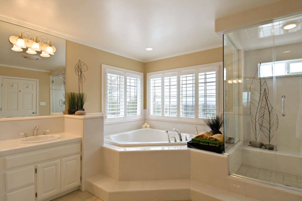 Murs de couleur beige avec une section de baignoire bien éclairée, un meuble-lavabo en bois blanc et une section de douche aux parois de verre