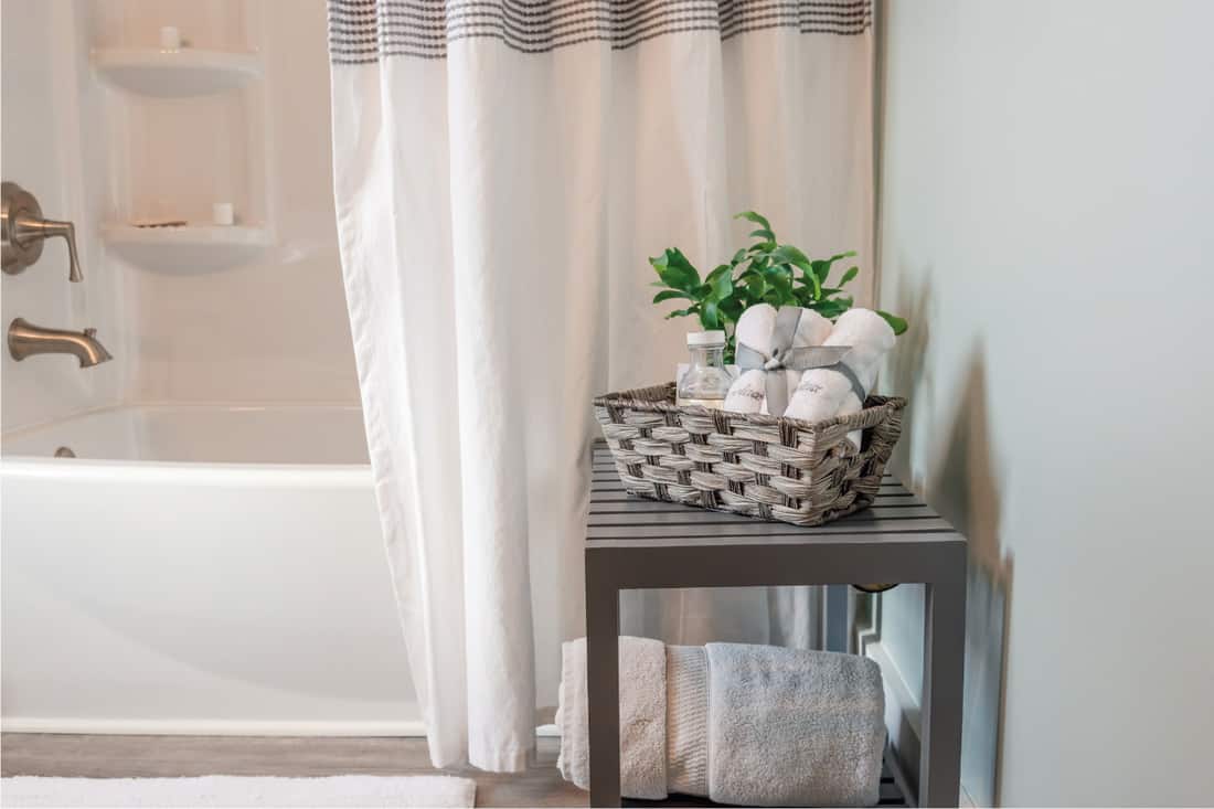 Clean and bright bathroom with table beside tub and shower curtain going outside the bathtub