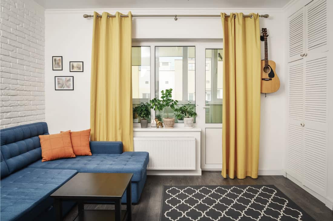 Chambre familiale propre avec canapé bleu, moquette grise et rideaux jaunes