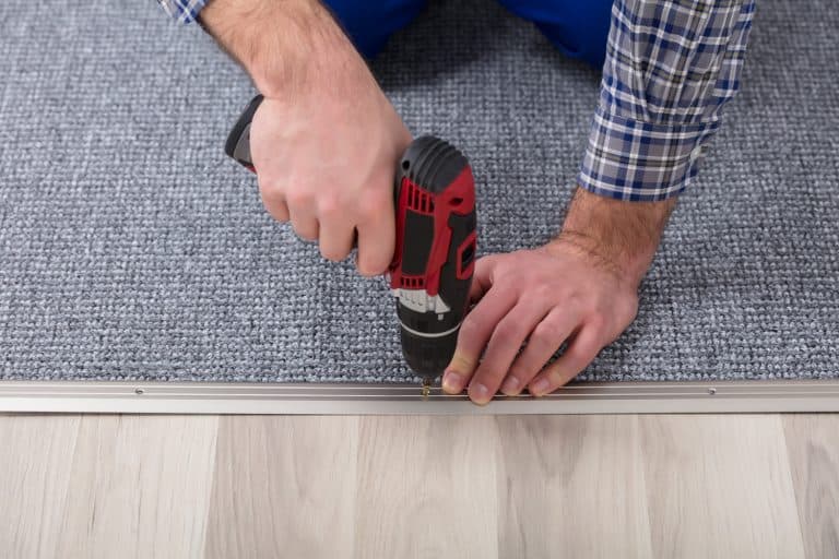 How To Keep Carpet Edges From Fraying [6 Methods], Close-up Of A Carpet Fitter's Hand Installing Grey Carpet With Wireless Screwdriver