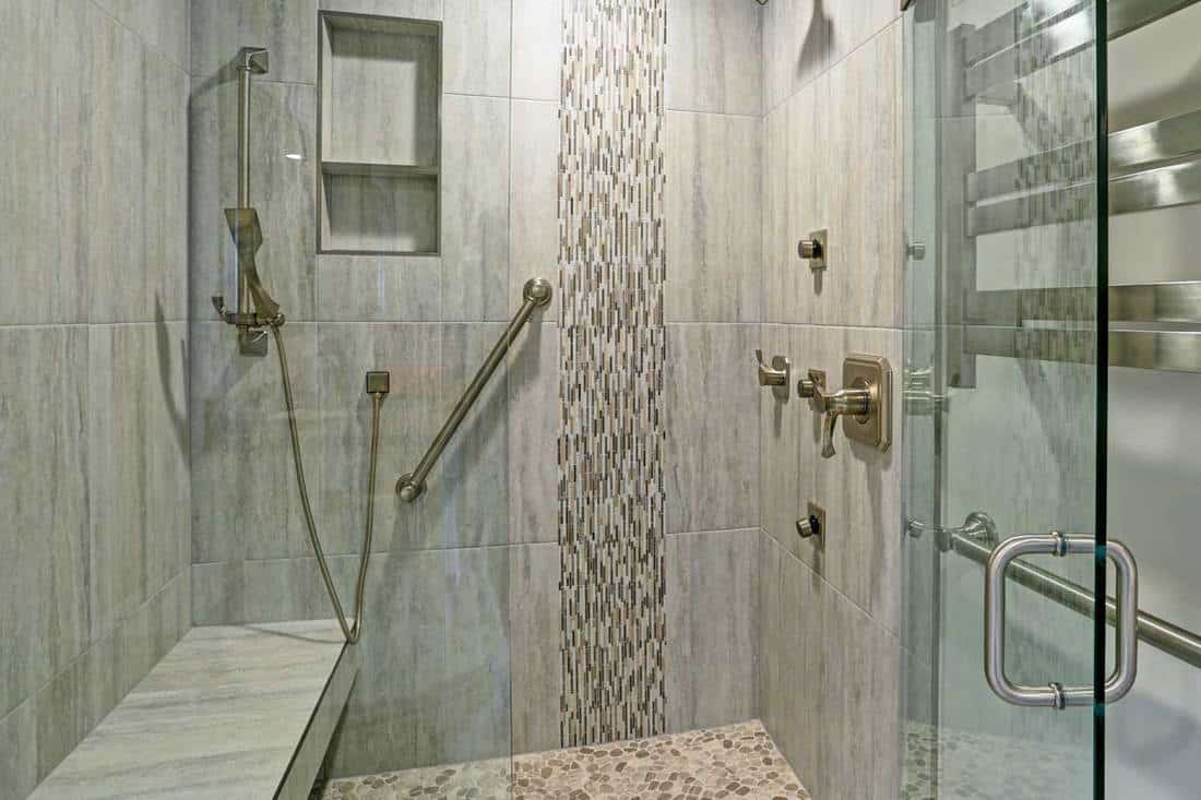 Contemporary bathroom design boasts gorgeous walk-in shower with tiled recessed shelves, built-in bench and accented with glass mosaic tiled vertical stripe, Can You Heat a Shower Bench?