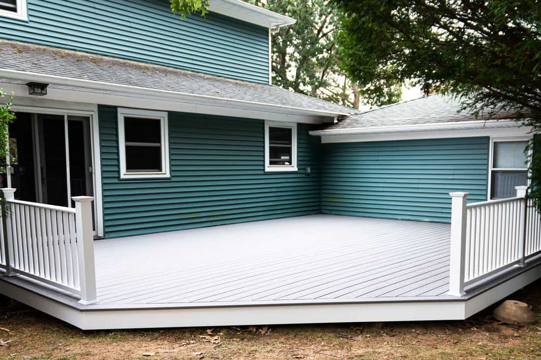 Exterior of a residential home with blue vinyl sidings and a composite deck on the backyard, How To Keep Spiders And Other Bugs Off Vinyl Siding