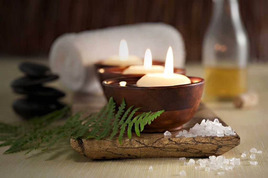 Bougies d'aromathérapie flottantes dans des bols en bois, pierres de massage et huile dans une ambiance spa zen