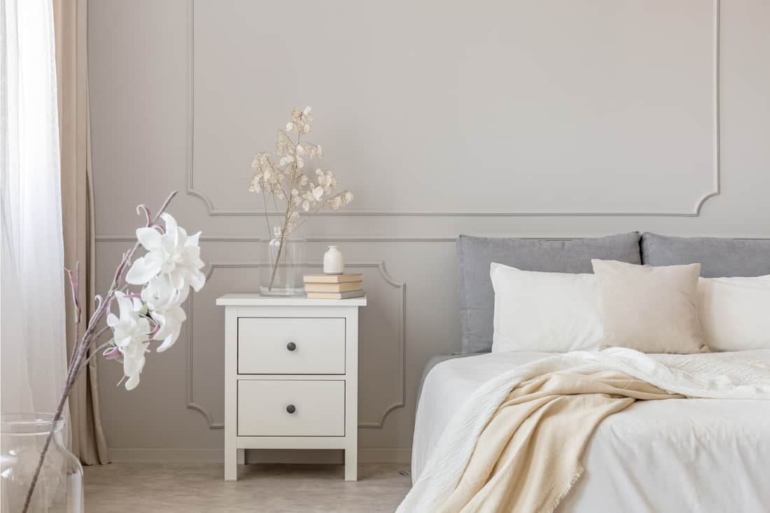 Flowers on nightstand table in delightful bedroom interior with gray and white design