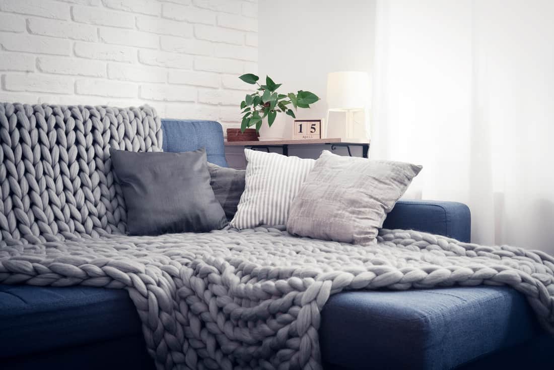 Gray knitted blanket from merino wool on couch with pillows in the interior of the living room
