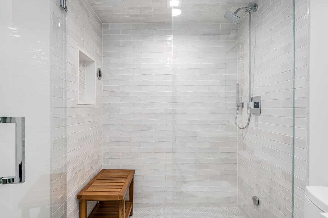 Gray tiled shower enclosure with glass doors and bamboo bench